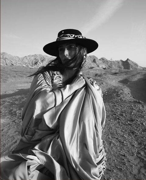 Dasha Savitskiy, founder of SAVVY VISION, in a wide-brimmed hat and silk wrap in the desert